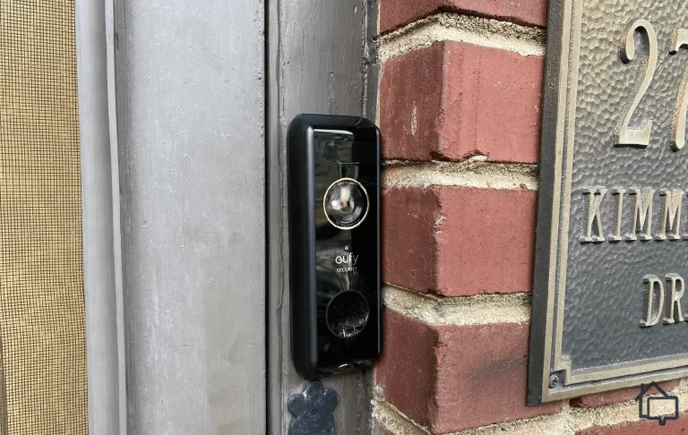 eufy Security video doorbell mounted on a grey door frame beside a red brick wall