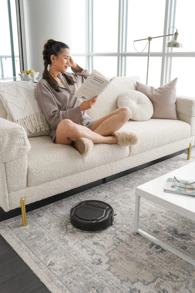 Lefant robot vacuum cleaning a rug while a woman reads on the sofa
