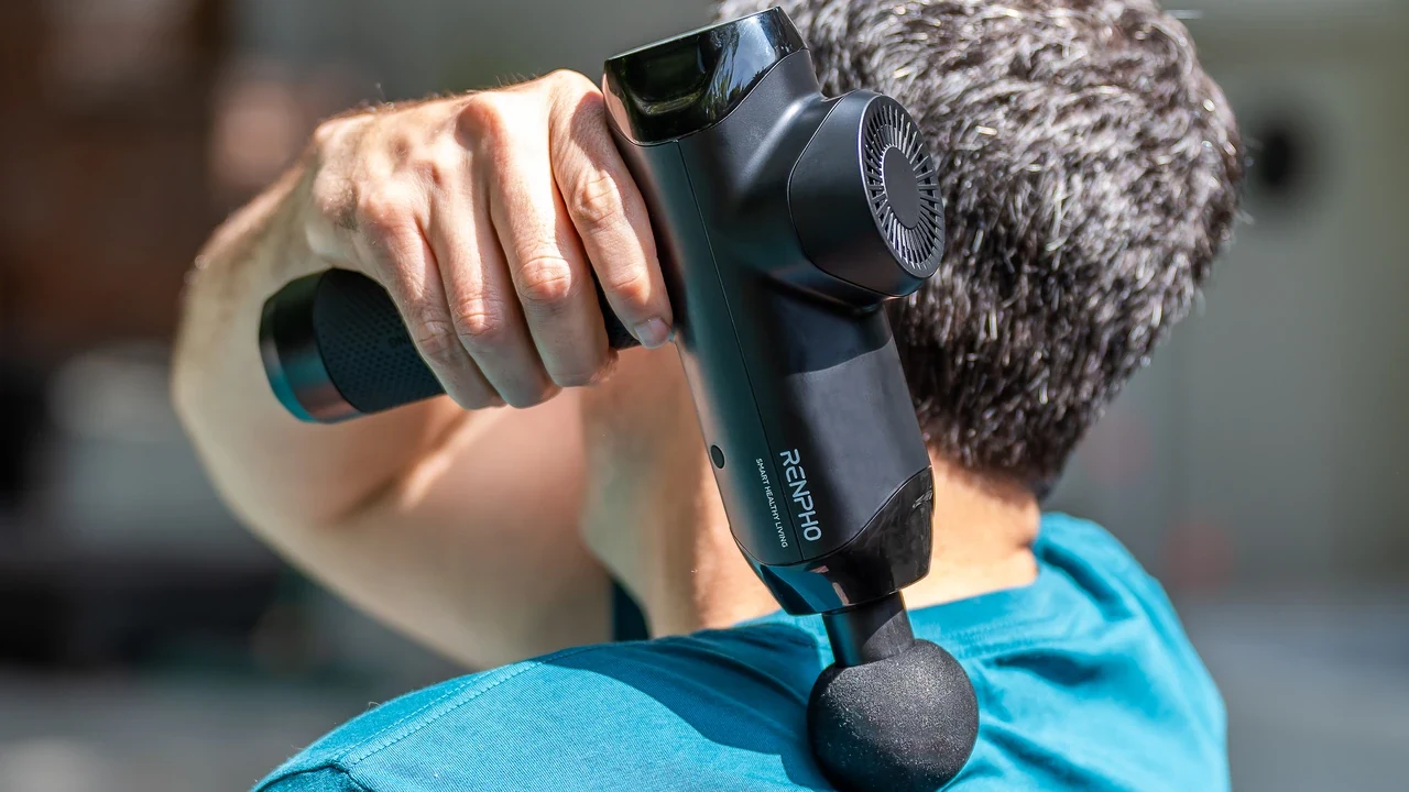 Person using a RENPHO massage gun on the upper back outdoors