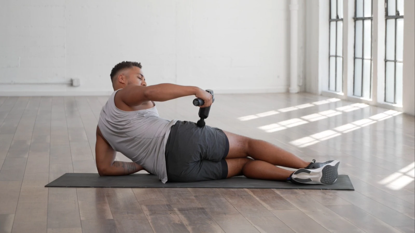 Man using a RENPHO massage gun on the hip while lying on a yoga mat